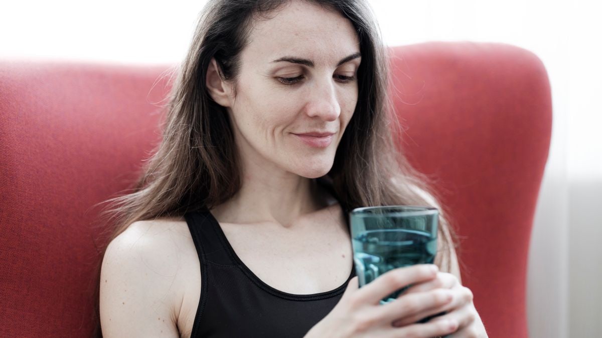 A relaxed woman in black top holding a glass of water and smiling, sitting indoors.