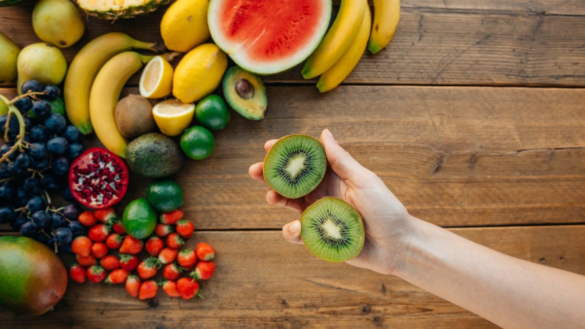 A vibrant assortment of fresh fruits on a wooden table, featuring a hand holding sliced kiwi, perfect for health and lifestyle themes.